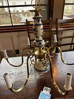 Front angled view of the blue and white ceramic chandelier showing the central body and six brass arms ending in light sockets.