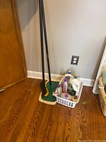 Full view of the lot showing green hardwood floor mop with white cloth attached, black-handled brush, and small plastic basket filled with assorted cleaning bottles.