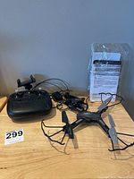 Drone and controller on wooden surface, manuals wrapped in plastic behind.