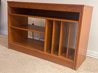 Wood entertainment center shown from angle with shelves and media dividers visible.