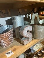 Four galvanized metal baskets and a metal 'S' displayed on a wooden shelf, showing shape and condition including rust spots on the baskets.