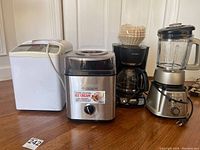 Four kitchen appliances including Hitachi bread maker, Cuisinart ice cream maker, Mr. Coffee coffee maker with paper filters, and Cuisinart blender/food processor.