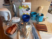 Photo of kitchen utensils, appliances, molds, storage containers and miscellaneous kitchen tools arranged on a table showing various items