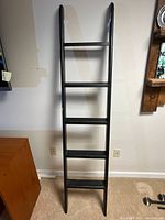 Full view of black wooden library ladder leaning against wall showing five rungs and ladder width.