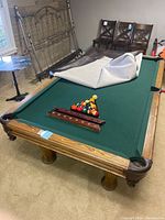 Full view of pool table with felt partially removed showing green surface and wooden base; triangle and balls on table