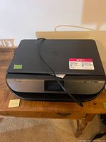 Top exterior side view of the black HP Envy 5055 printer with top lid closed and power cable resting on it.