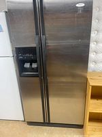 Full front view of the Whirlpool stainless steel side-by-side refrigerator and freezer with water and ice dispenser on left door.