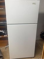 Closed full view of white top-freezer refrigerator with Kirkland Signature label on top right corner of freezer door.