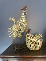 Front and side angles of rooster and hen metal baskets showing woven metal designs, painted beaks, and detailed features.