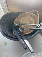 Two woven serving baskets (dark and light) with metal salad serving utensils on top.