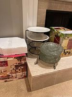 Photo showing the packaged 4-tier buffet server, glass plates stacked on a metal stand, and boxed beverage dispenser.