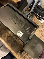 Black metal adjustable laptop stand viewed from an angle showing the perforated laptop platform and attached mouse pad extension.