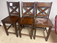 Three counter height stools made of dark stained wood with X-back design, placed side by side showing general condition and appearance.