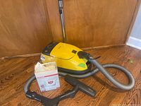 Yellow Miele vacuum on hardwood floor with corrugated hose, floor nozzle and box of replacement bags