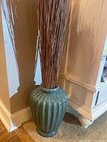 Green ceramic ribbed vase filled with thin brown faux sticks placed on floor corner