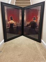 Two framed Brett Lynch bar scene paintings positioned corner to corner on a carpeted stair landing, showing full view of both artworks in black frames.