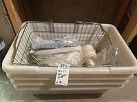 Stack of 4 white plastic storage bins with metal wire grocery basket on top containing deli supplies like wrapped twine, plastic bags, meat hooks.