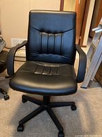 Front view of black leather office chair showing padded seat, backrest with vertical stitching, and armrests.