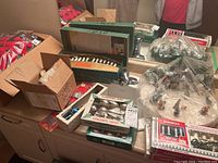 Photo showing the assortment of vintage Christmas items including boxes of glass ornaments, packages of string lights, and parts of the village scene.