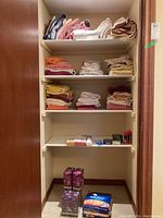 Full view of bathroom closet with neatly stacked folded towels mostly on top three shelves, and small toiletry items on fourth shelf, unopened boxes on bottom shelf.
