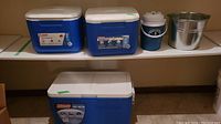 Photo showing three coolers and one metal pail displayed on a white shelf