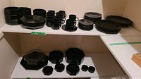 Full lot showing multiple black octagonal plates, mugs, and bowls arranged on shelves.