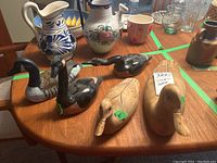 Wood carved duck and goose sculptures arranged on a table with other pottery and glass items in the background.