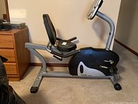 Side view of the Cycle PEC-4920 recumbent exercycle showing padded seat, backrest, pedals with straps, and digital display.