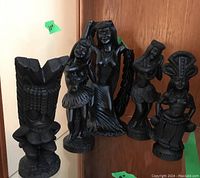Five black carved Hawaiian figurines displayed on a glass shelf, showing varied poses and traditional Hawaiian attire