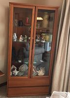 Full front view of teak cabinet showing glass doors, interior contents and two lower drawers