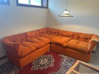 Orange two-piece sectional sofa with five loose seat cushions in basement setting