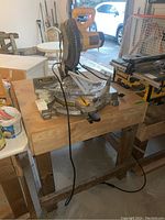 Front view of DeWalt miter saw mounted on wooden table with power cord hanging