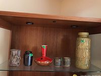 Full view of six pottery pieces displayed on a shelf including vases and cups with various shapes and colors