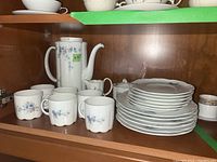 Porcelain coffee set arranged on shelf including stack of saucers, coffee pot, cups, creamer, and sugar bowl with Classic Rose floral pattern