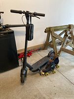 Full view of Red Sky electric scooter standing next to quad roller skates in garage