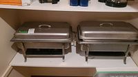 Front view of two stainless steel chafing dishes with lids on shelf