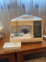 Kenmore 18 sewing machine in off-white color wrapped in plastic with power cord and foot pedal included.