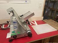 Side view of Nella slicer on red bench with power cord and mineral oil bottle in foreground