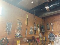 Wall with assorted tools and hardware mounted including wrenches, clamps, drill bits, rulers, nails, and lock nuts.