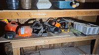 Shelf holding various yard tools and equipment including gas can, hard hat, planter hangers, chainsaw, and other tools.
