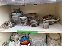 Full view of top shelf showing stacks of plates, bowls, and the lidded serving bowl, along with smaller cups and sauce dishes