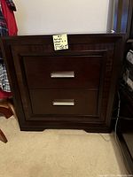 Front view of one dark wood bedside cabinet with two drawers and metal handles, showing overall structure and design