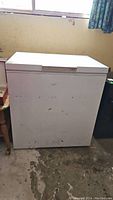 Full front view of the white chest freezer showing its rectangular shape and signs of wear.