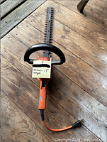 Front view of orange electric hedge trimmer laid flat showing full length including blade, handle, and power cord, with a sticky note indicating 'metal - 17 inch length'.