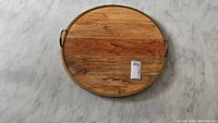 Top view of round wooden lazy susan with brass-like rim and handles showing wood grain and some stains.