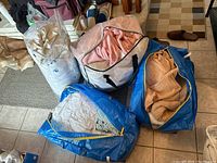 Image showing several packed linen bags including a transparent bag with white linens, blue IKEA bags with blankets and towels, and a pink blanket in a clear storage bag.