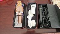 Two microphones in black carrying case: a gold Mangbangkorea V12 microphone with charging cable and manual, plus a black Intergolf Pro 188 wired microphone with cable.