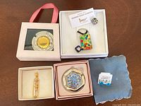 Photo shows Murano glass earrings, pendant necklace with colorful glass elements, two foldable handbag holders, and packaging boxes on a wooden surface.