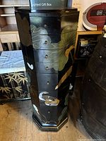 Front view showing black lacquered surface with Oriental leaf and butterfly motifs on 8 drawers, circular drawer knobs, with light marks and wear visible.