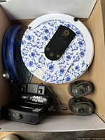 Top view of robot floor cleaner with accessories including charger, dustbin, and small parts in box.